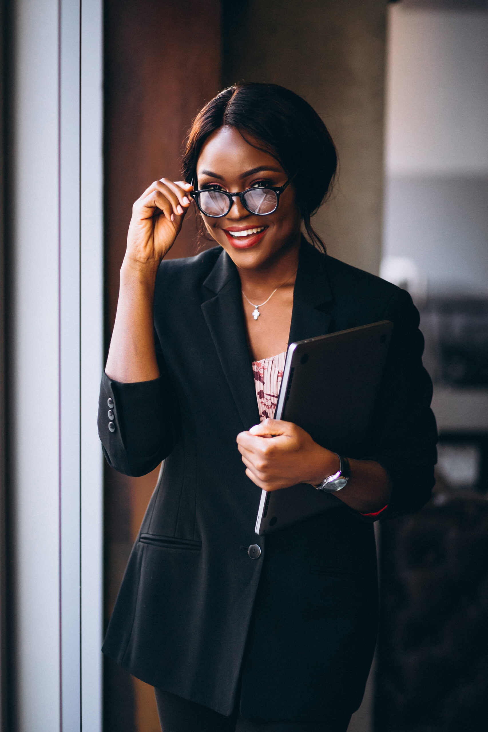 African american business woman holding laptop and standing by the window
